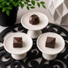 Three espresso-inspired artisan bonbons displayed on white pedestal stands, featuring Espresso, Baileys & Coffee, and Espresso Martini flavors handcrafted by Bomb Confections.