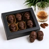 Bomb Confections 6-piece bourbon chocolate skull assortment handcrafted with creamy bourbon-infused chocolate and filled with whole almonds or pecan halves, presented in a premium black window gift box with a crystal whiskey glass and Buffalo Trace bourbon for an upscale cocktail-inspired presentation.