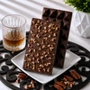 Bomb Confections Bourbon Chocolate Bar showing the smooth geometric front alongside the optional chopped pecan back, displayed with subtle Buffalo Trace bourbon accents and pecans.
