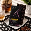 Bomb Confections Bourbon Chocolate Bar in premium gift packaging displayed with the artisan chocolate bar on a white pedestal, accented by Buffalo Trace bourbon and pecans.