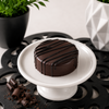 Dark chocolate covered sandwich cookie finished with glossy dark chocolate drizzle and displayed on a white pedestal in a clean boutique dessert setting.