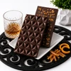 Bomb Confections Old Fashioned Bourbon Chocolate Bar showing the geometric chocolate front alongside the back topped with chopped candied orange peel, displayed with Buffalo Trace bourbon and candied orange accents.