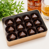 Buffalo Trace Bourbon Bonbon Gift Tin by Bomb Confections featuring 12 handcrafted bourbon bonbons presented in a premium copper gift tin with a crystal whiskey glass and Buffalo Trace bourbon for an elegant gourmet chocolate gift.