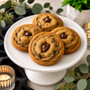 Handcrafted bourbon chocolate chunk cookies displayed on a white pedestal with eucalyptus, black accents and elegant event décor.