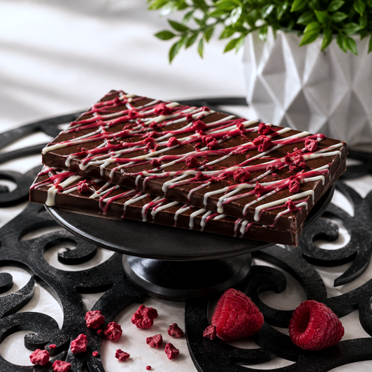Handcrafted Raspberry Daiquiri Rum Chocolate Bar by Bomb Confections featuring rich dark chocolate with freeze-dried raspberry pieces and raspberry-white chocolate drizzle, displayed with fresh raspberries in a premium boutique presentation.