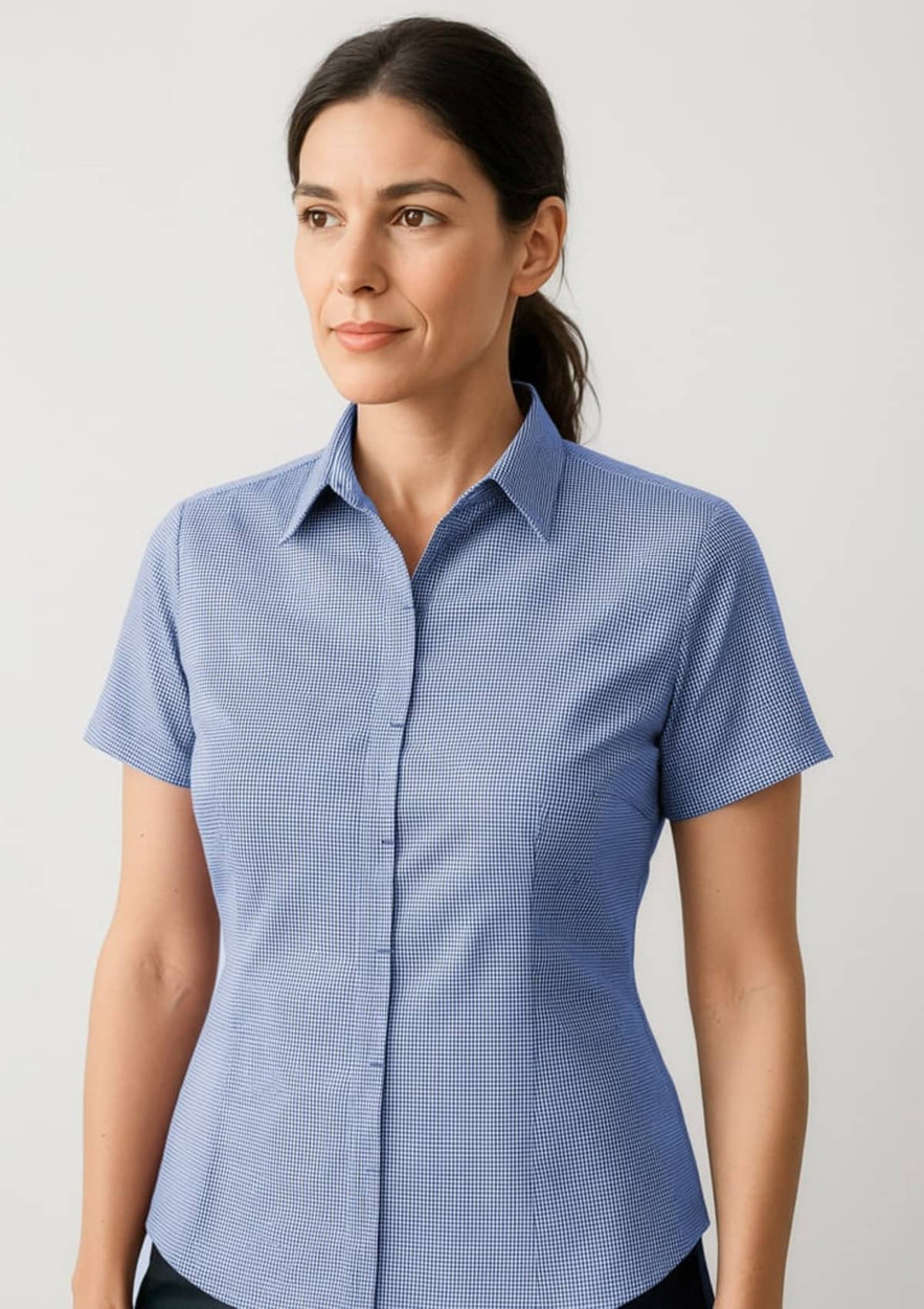 A short-sleeve button-up shirt in light blue, featuring a checkered pattern and a collar. It has a logo on it.