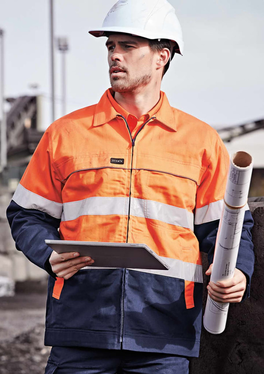 A man wearing a high-visibility orange and navy jacket, holding a notebook and rolled plans, with a hard hat on.