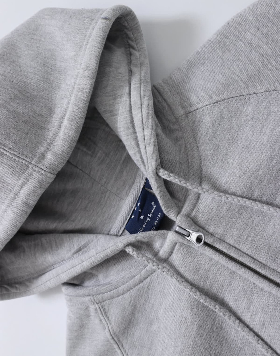 A grey full-zip fleecy hoodie featuring a hood and stitched detailing, with branding visible inside.