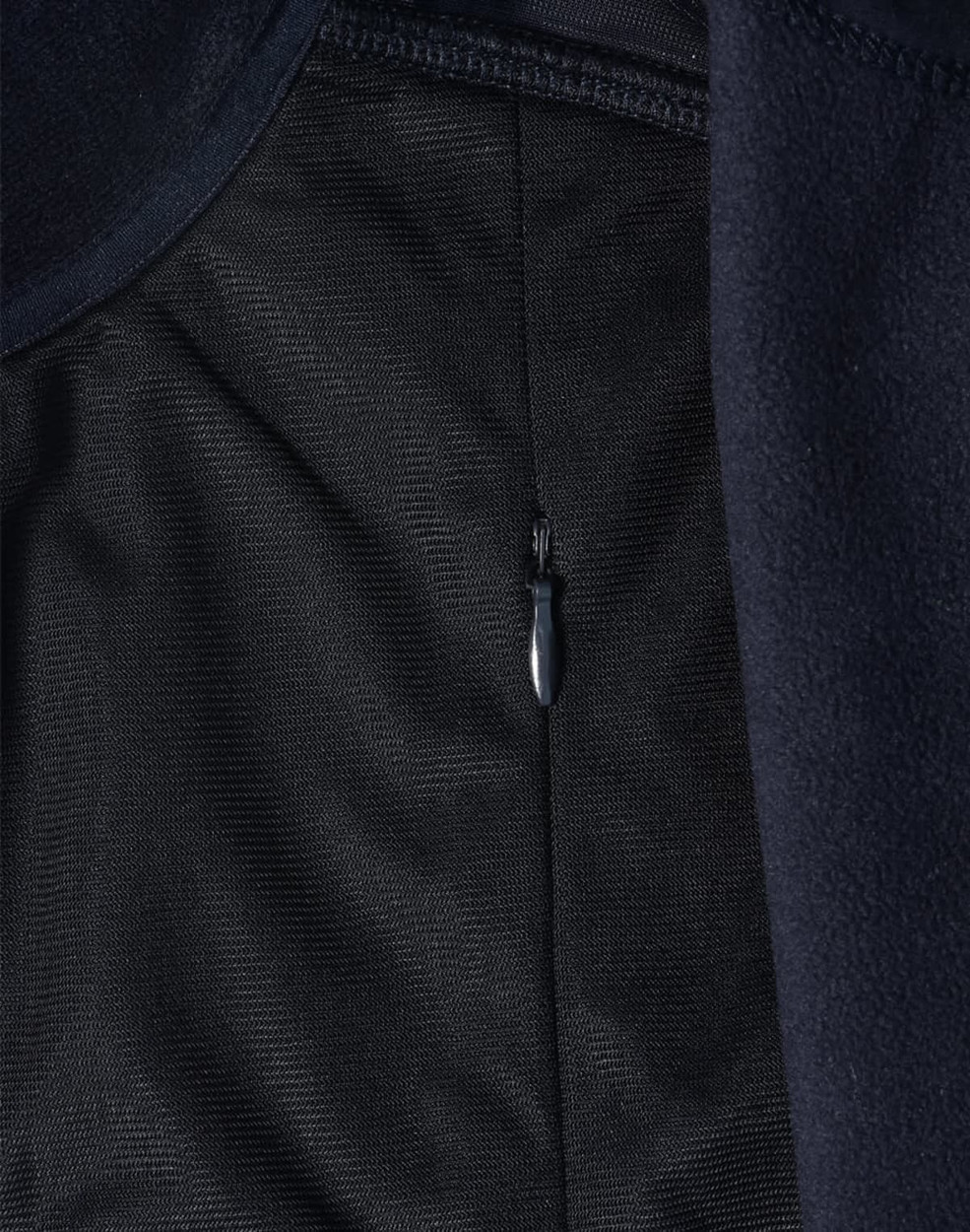 A close-up of a navy blue softshell jacket, featuring a zippered pocket and textured fabric.