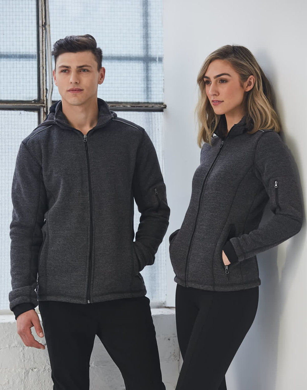 A black heather bonded fleece jacket displayed on models, featuring a zip front and pockets.