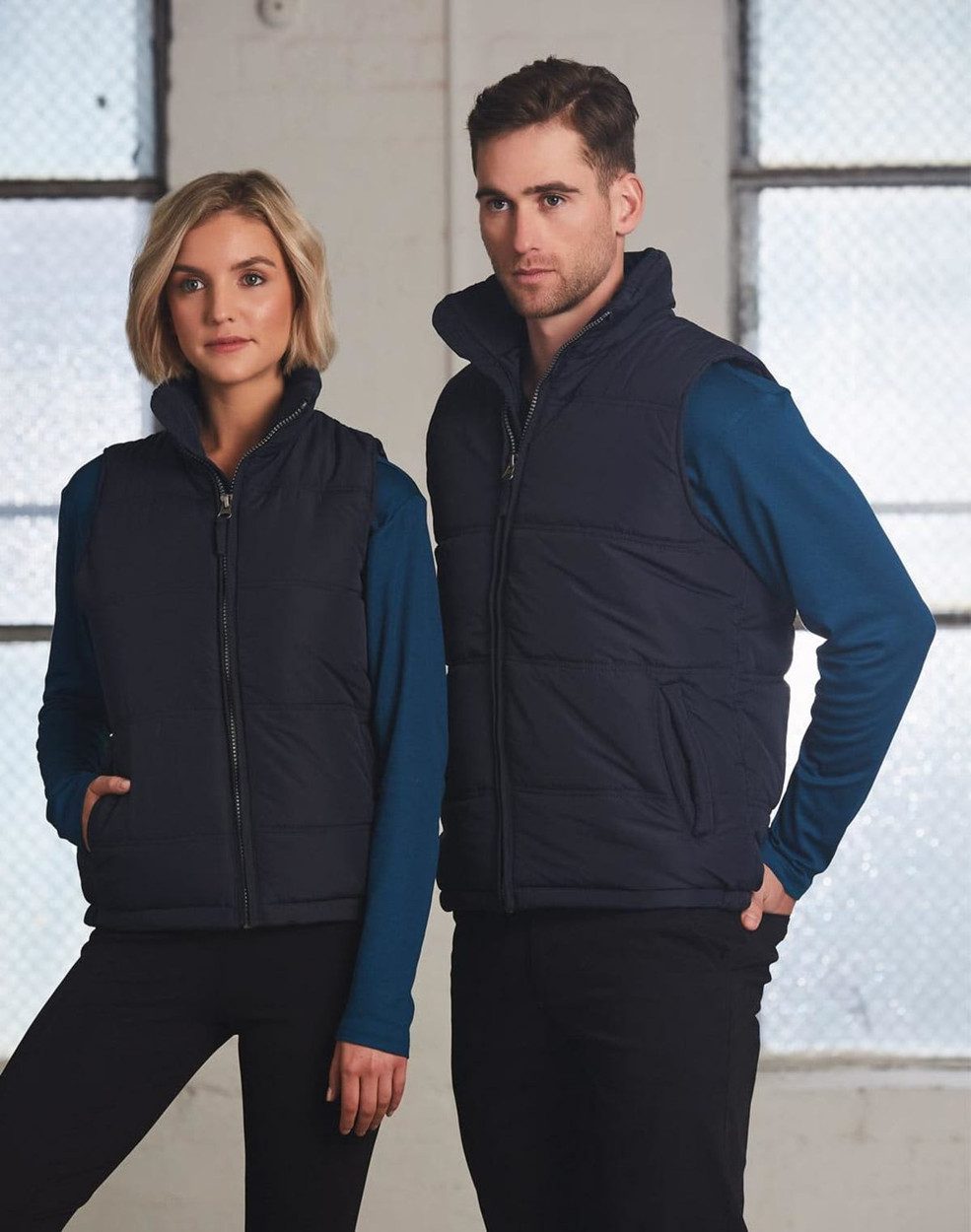 A navy blue heavy quilted vest is worn by a male and female model against a light backdrop, featuring a logo.