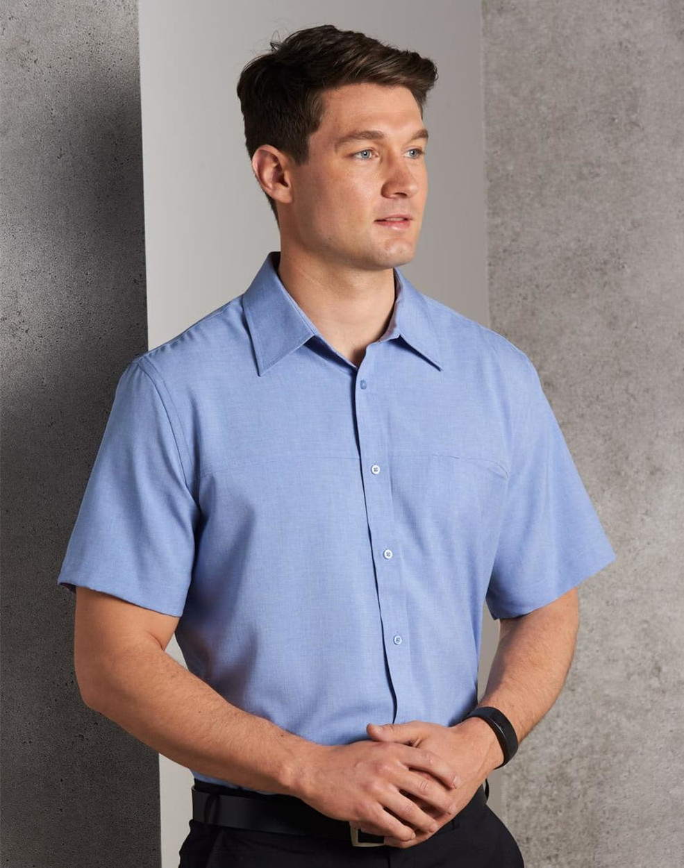 A short-sleeve men's shirt in light blue with a button-down front and a chest pocket, featuring a logo.