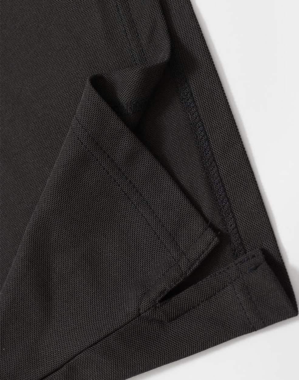 A close-up of a black polo shirt featuring a neatly stitched hem and collar. The fabric texture is visible.