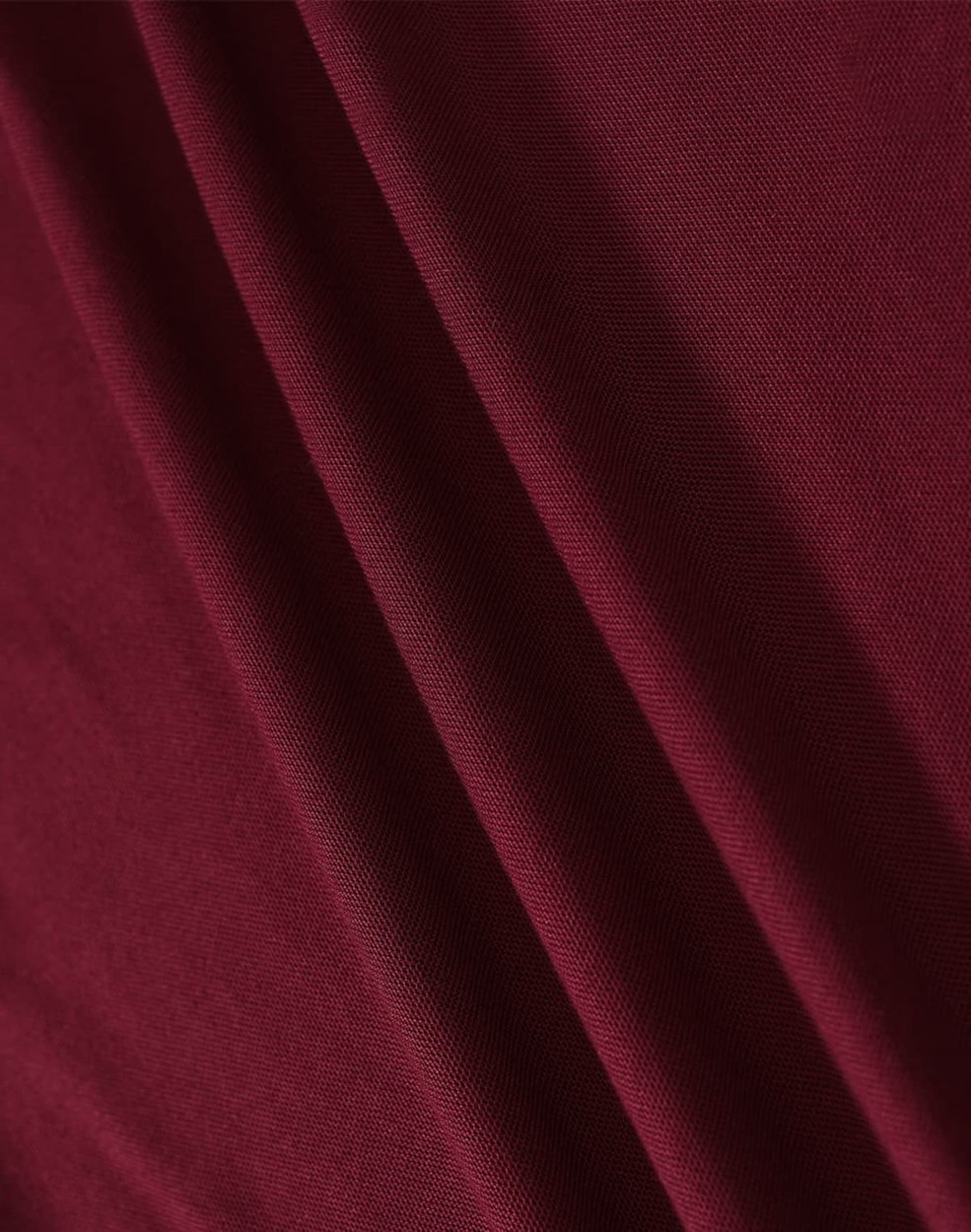 A close-up of a textured fabric in a rich burgundy colour, showcasing its drape and weave.