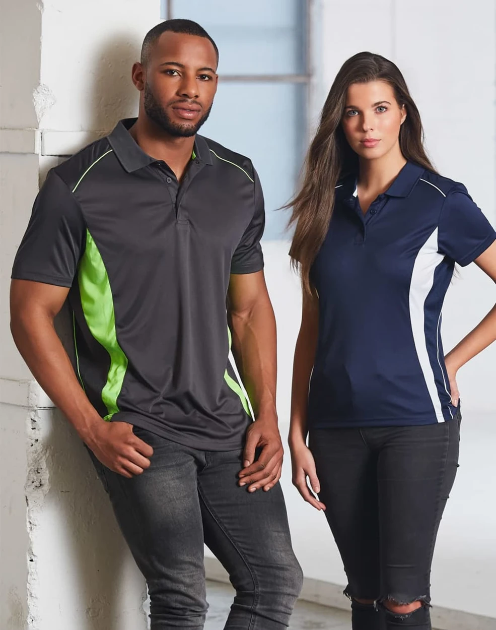 A grey polo shirt with green accents worn by a man, and a navy polo shirt with white accents worn by a woman. Both have logos.