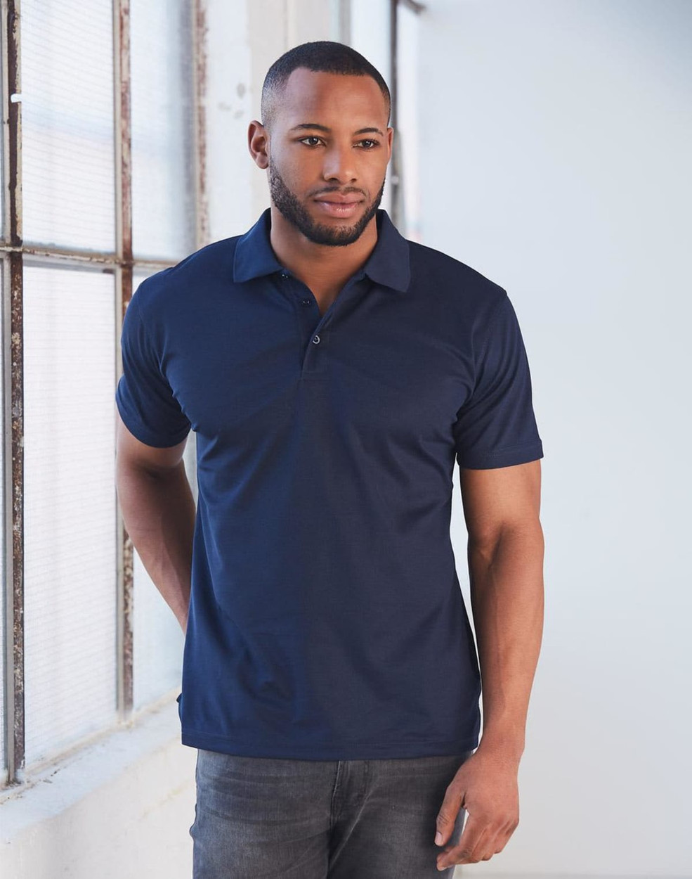 A man models a navy blue short-sleeved polo shirt, featuring a collar and a logo on the chest.