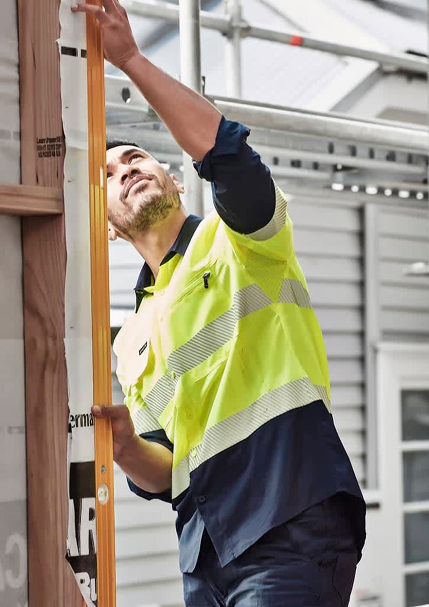 A man wearing a high visibility segmented tape long sleeve shirt in yellow and navy, working on a construction site.