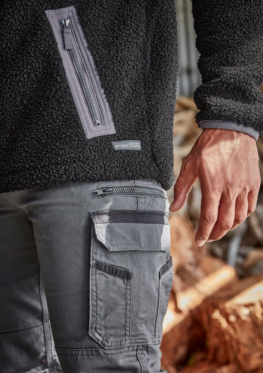 Unisex black Sherpa fleece with zippered pocket, paired with grey work pants featuring cargo pockets and branding.