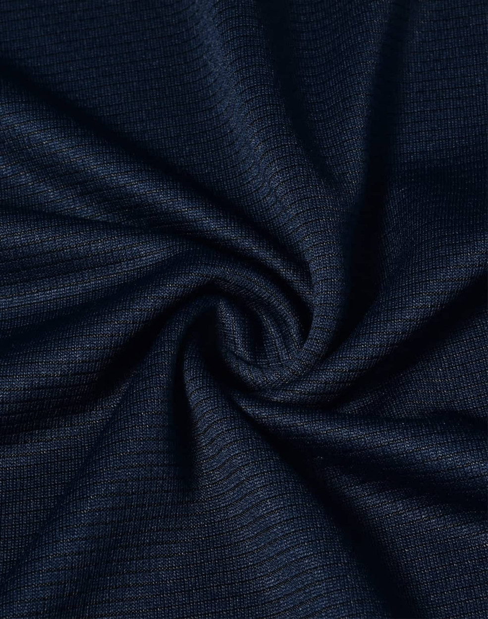 A close-up of navy blue textured fabric, displaying a smooth, lightweight weave. The fabric has a logo present.