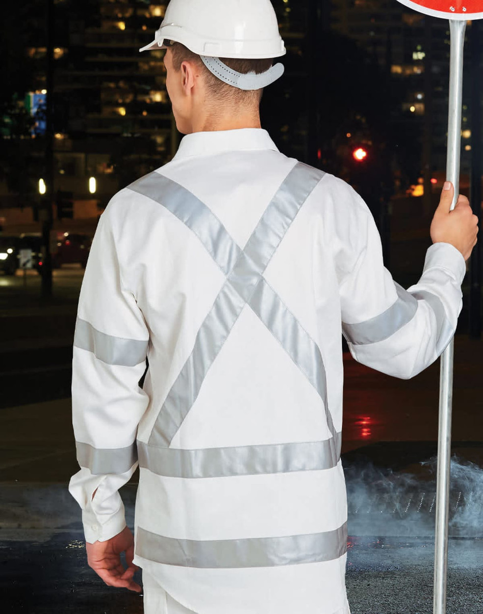 A safety shirt in white with reflective silver stripes, worn by a person holding a stop sign.