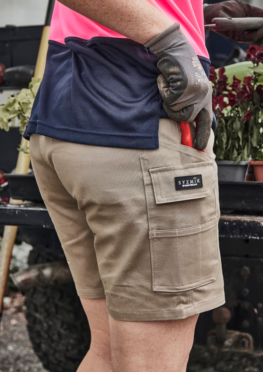 A person wearing khaki women's cargo shorts with a logo, holding gardening tools and dressed in a pink and navy top.