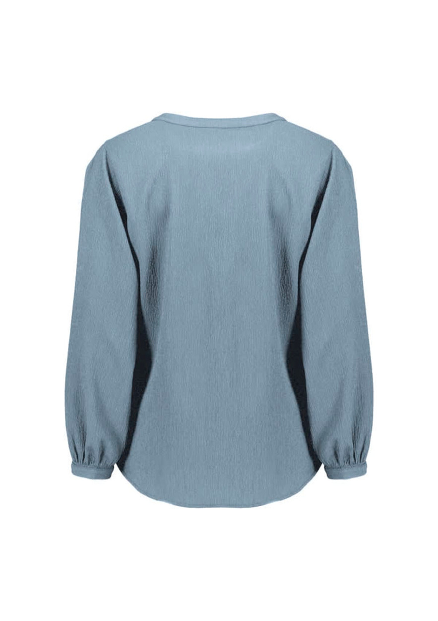 A women's long sleeve blouse in light blue, featuring a ruché design and a relaxed fit. It has a logo on the back.