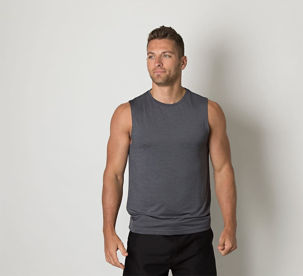 A grey sleeveless shirt is worn by a man standing against a plain background. The shirt features a logo.