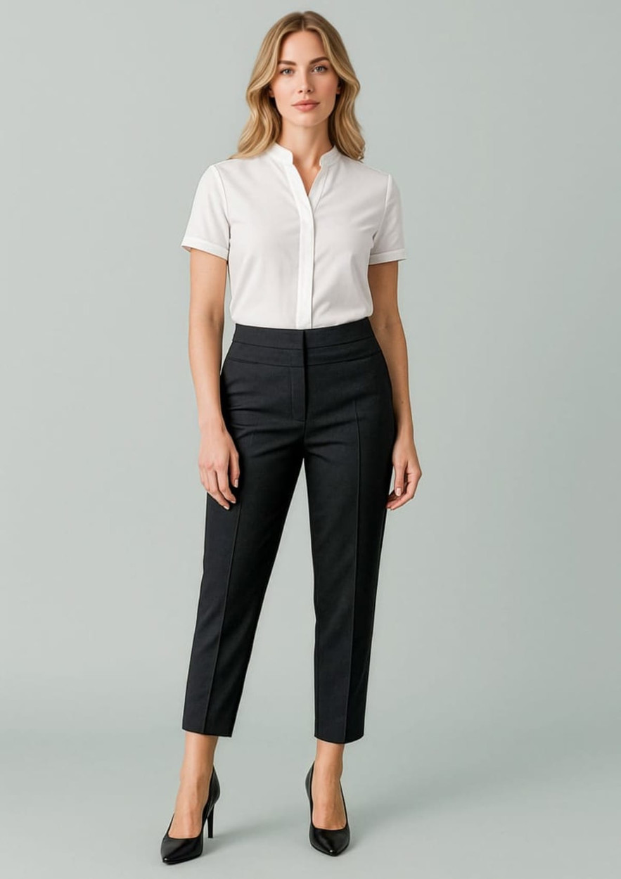A woman stands wearing a white shirt and black mid-waist slim leg pants with a branding logo, set against a pale background.