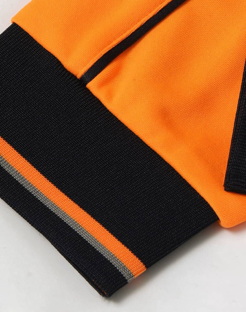A close-up of an orange and black long-sleeve polo shirt featuring a logo and contrasting cuffs.