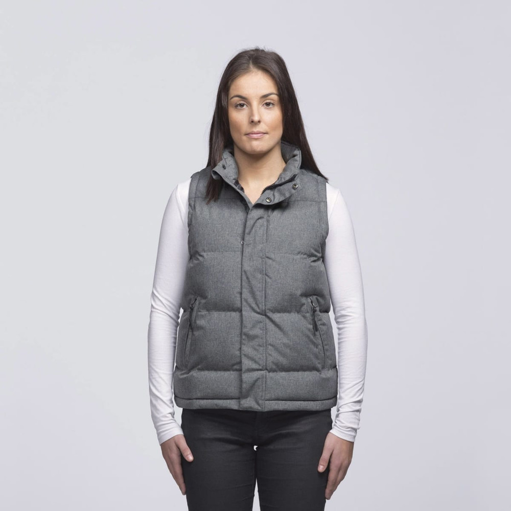 A grey puffa vest with a collar and pockets, worn over a white long-sleeve top. The model stands against a plain background.