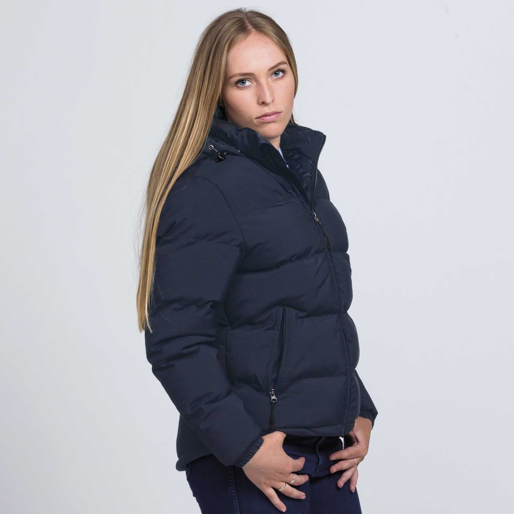 A woman wearing a navy blue puffer jacket, featuring a zip front and a high collar, with a logo visible.