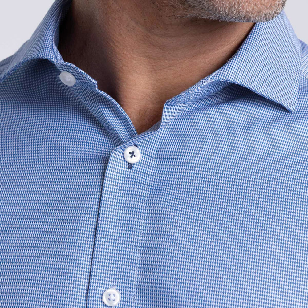 A close-up of a men's button-up shirt featuring a blue checkered pattern and white buttons. The shirt has a logo.