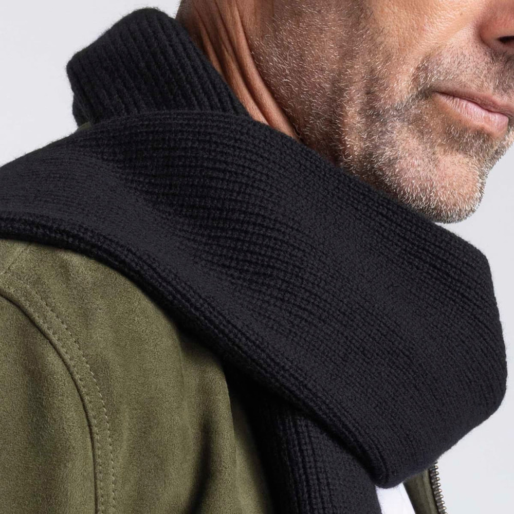 A black 100% Merino scarf with a textured knit, draped around the neck of a model.