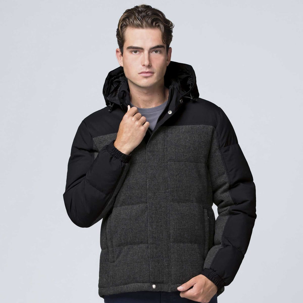 A man wearing a black and grey jacket with a hood, featuring a quilted design and elastic cuffs. There's a logo on the jacket.