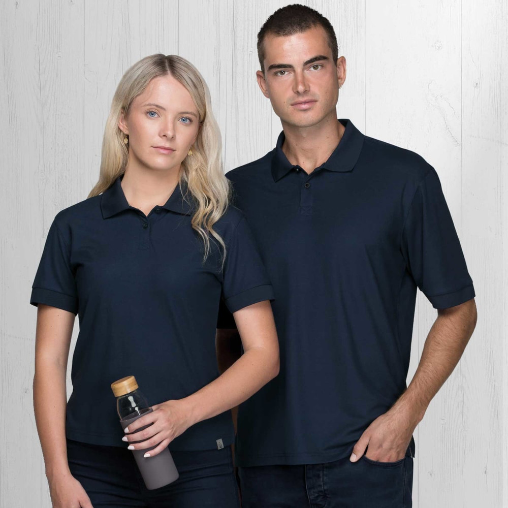 Two models wearing navy blue Dri Gear Renew Eco Polo shirts, one holding a drink bottle, against a light wooden background.