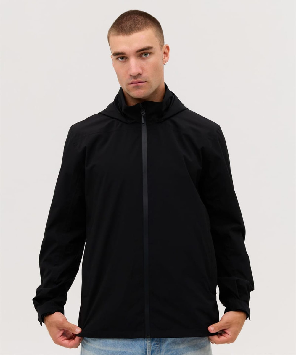 A black rain jacket is worn by a model, featuring a zip front and a hood. The jacket has a logo on it.