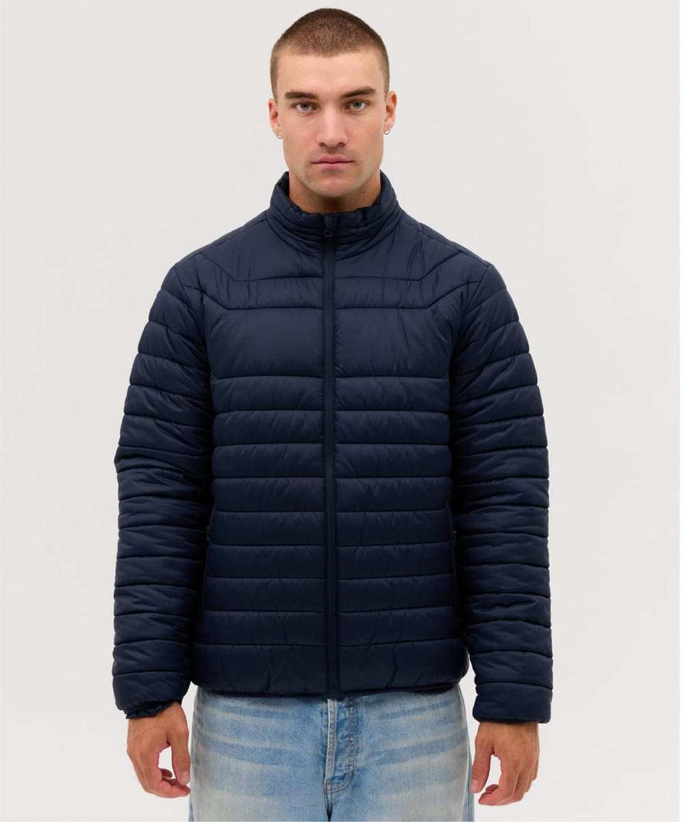 A navy blue puffer jacket with a zip front, featuring a high neck and padded design. The model is wearing light jeans.