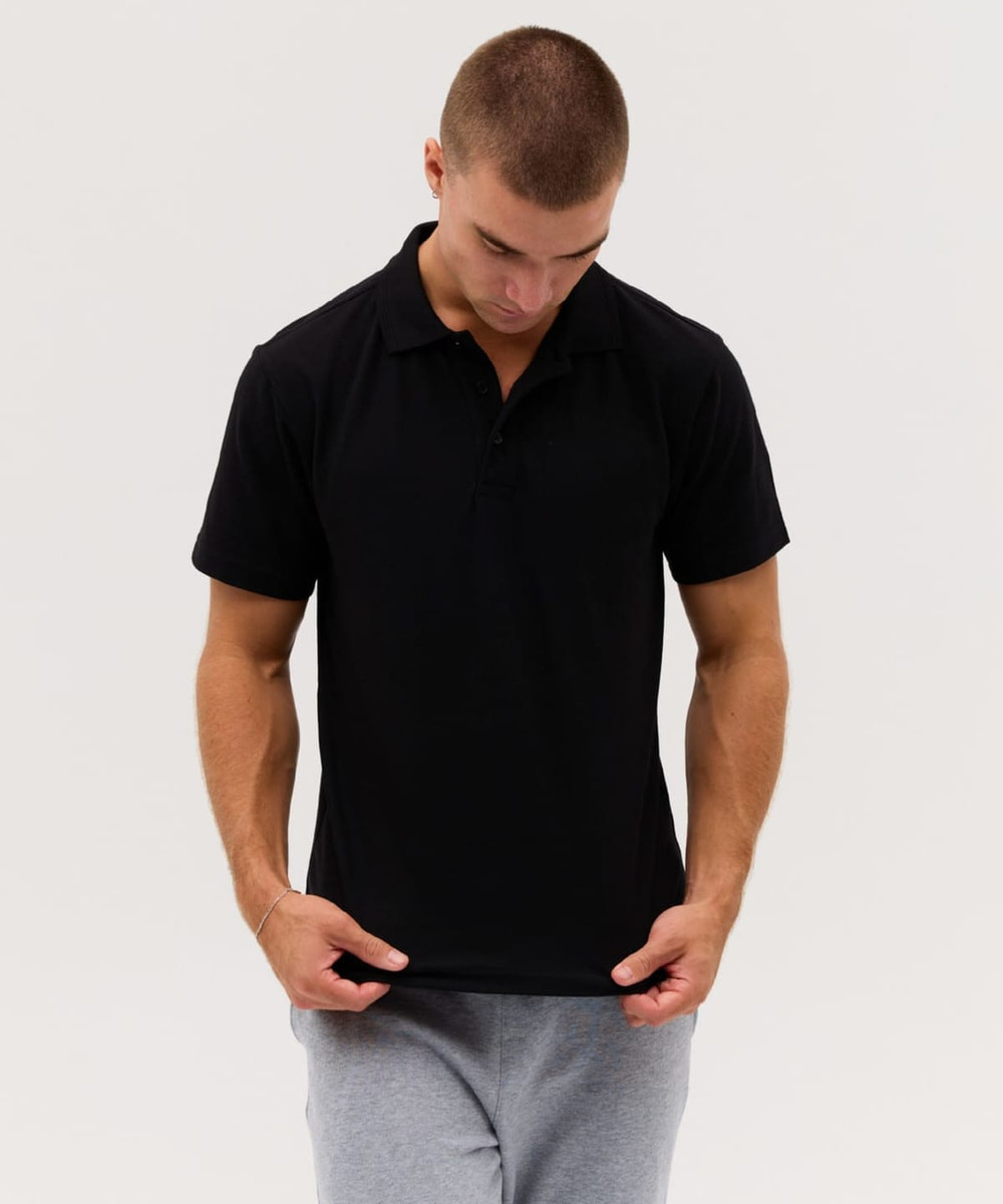 A black polo shirt featuring a logo, worn by a model in casual grey pants.