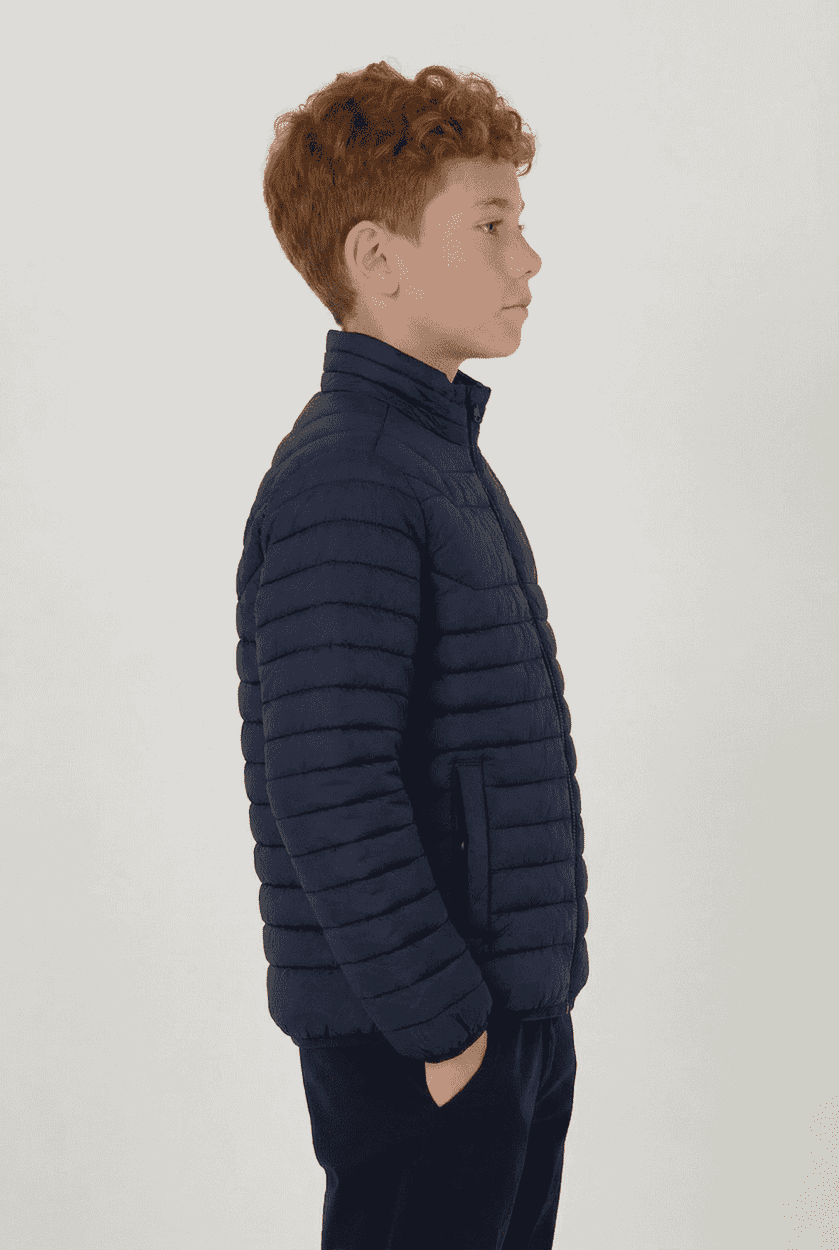 A side view of a young boy wearing a navy blue puffer jacket with a high collar and a logo on the chest.