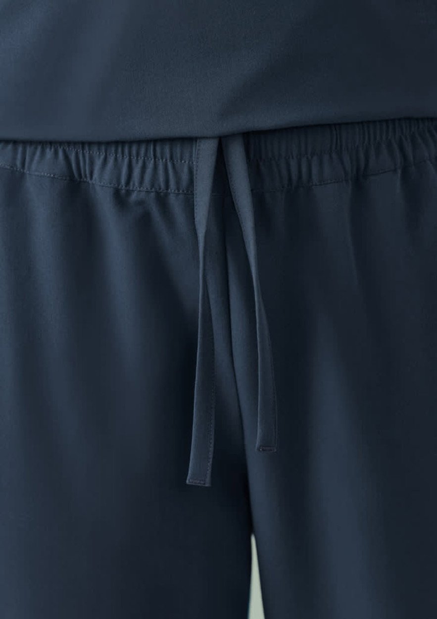 A pair of navy unisex scrub pants with an elastic waistband and drawstring detail. Features a logo.