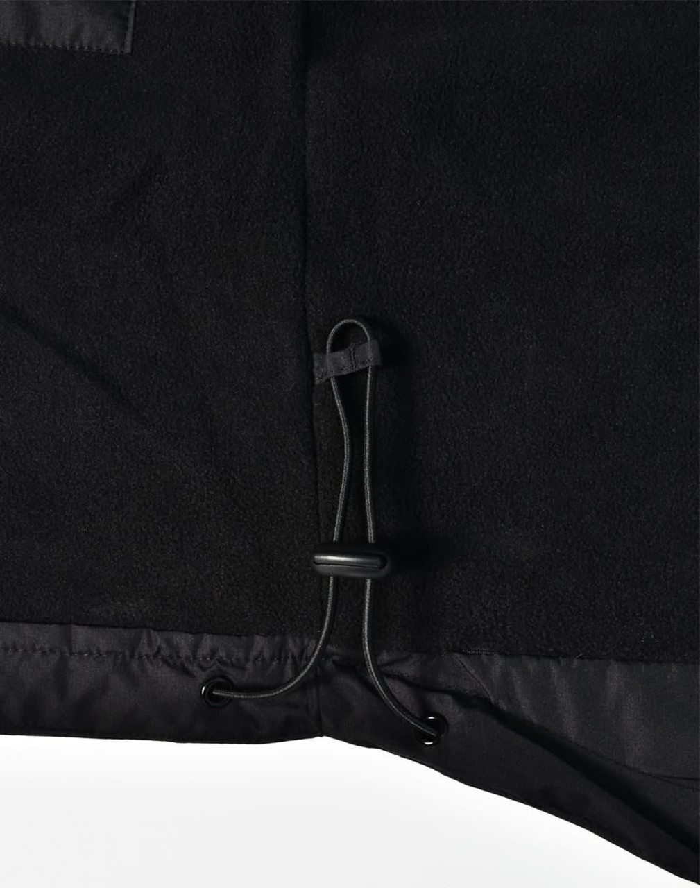 Detail of a black fleece jacket featuring a drawstring adjustment at the hem. The jacket has a logo.