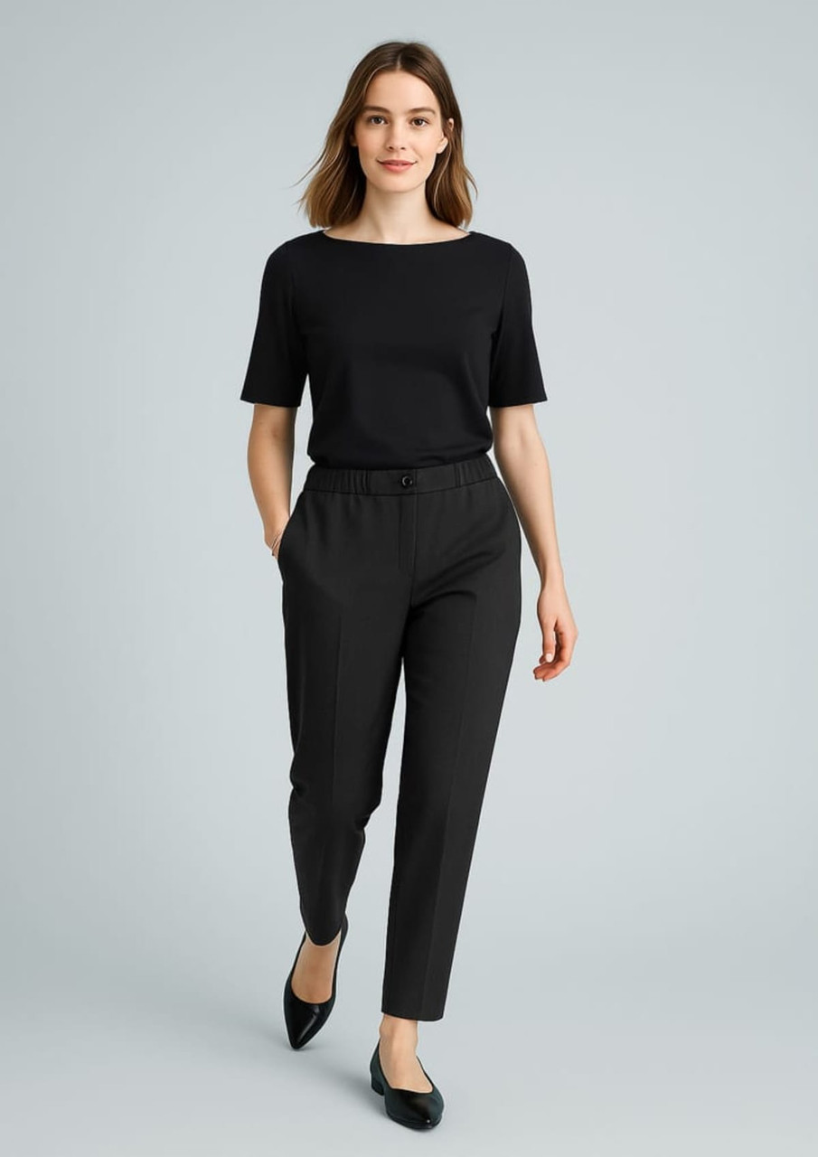 A woman wearing black slacks and a black top, walking confidently with her hands in the pockets of the pants.