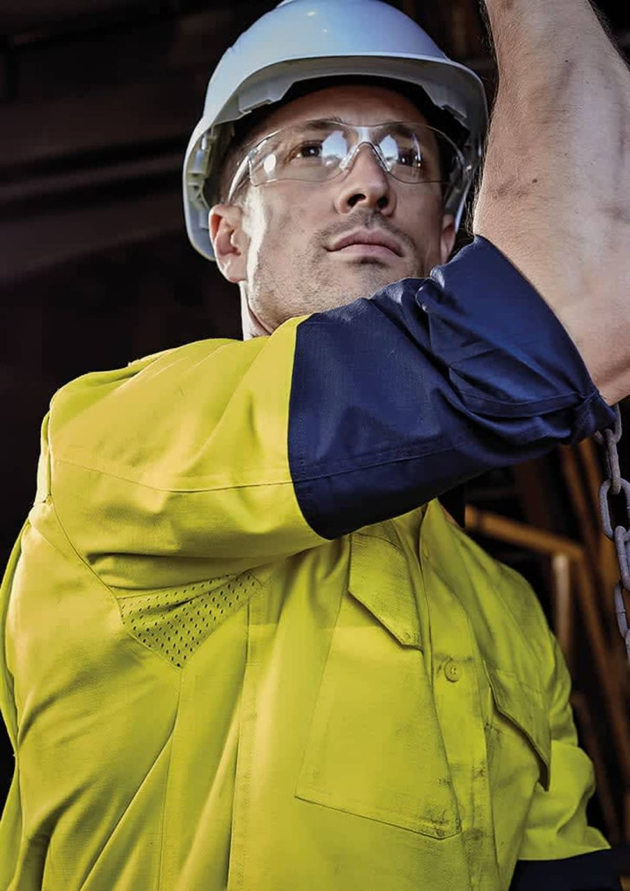 A men’s closed front long sleeve shirt in yellow and navy, featuring a logo, worn with safety goggles and a hard hat.