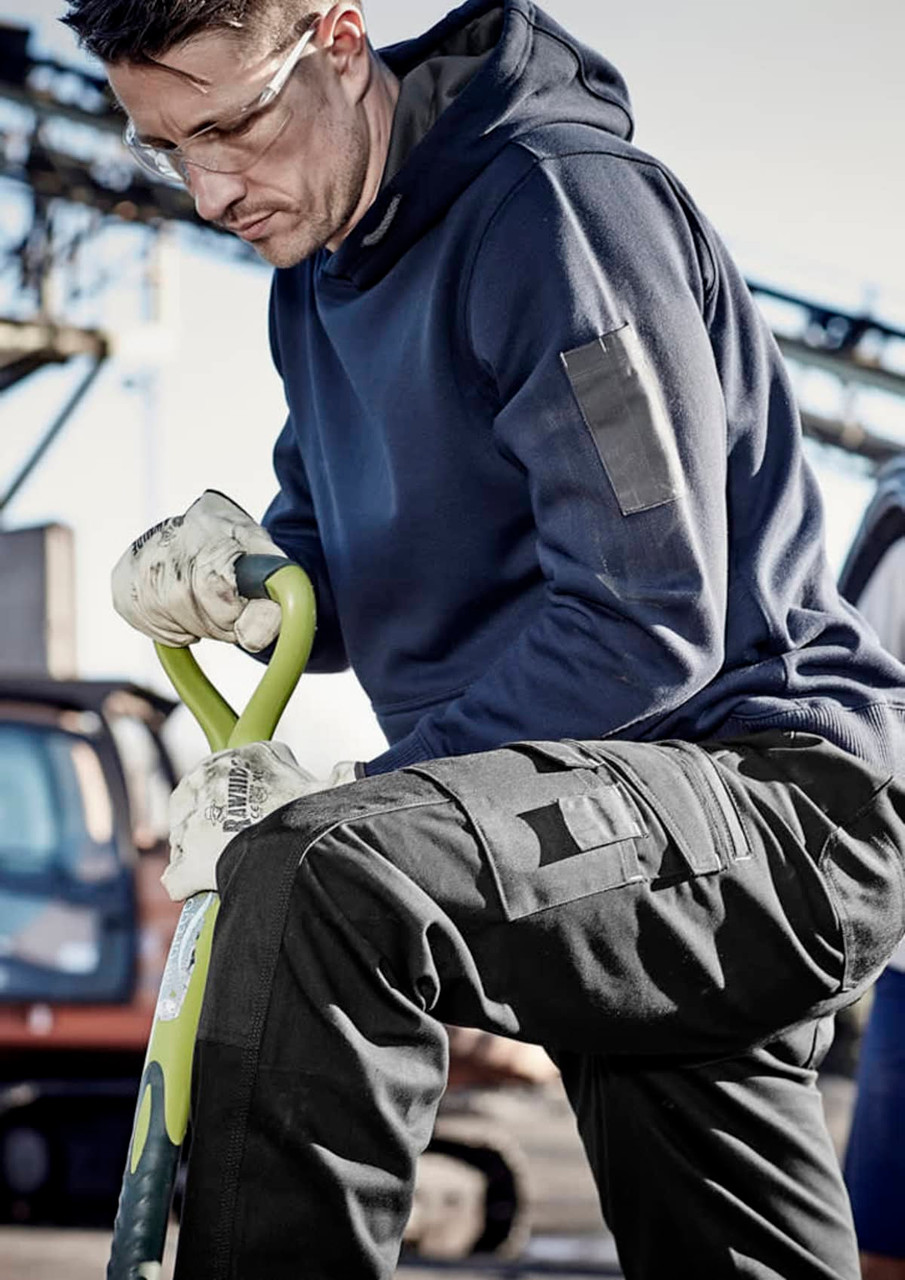 A man in a navy blue unisex multi-pocket hoodie, wearing gloves, kneels with a spade in a work environment.