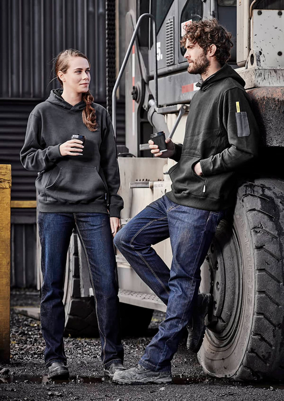 A pair of people wearing black hoodies and blue stretch denim work jeans, standing beside a large vehicle tire.
