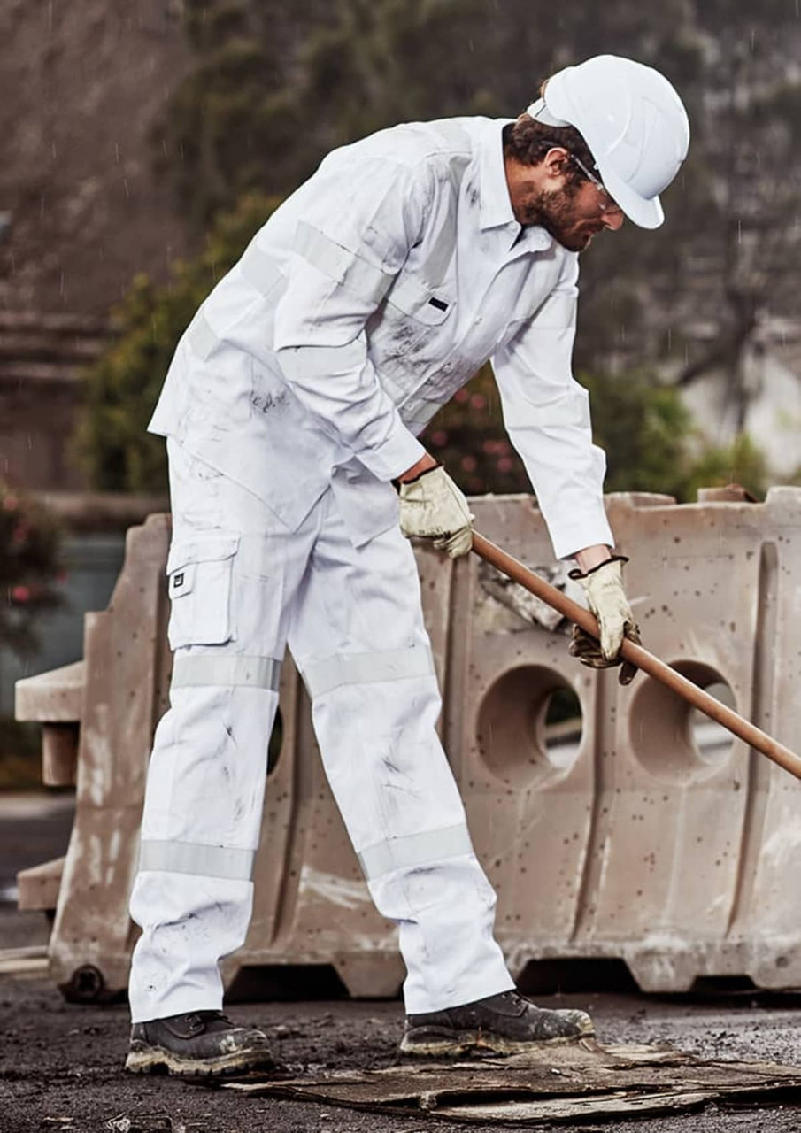 A man in white work pants is using a tool on a construction site, wearing a helmet and gloves.