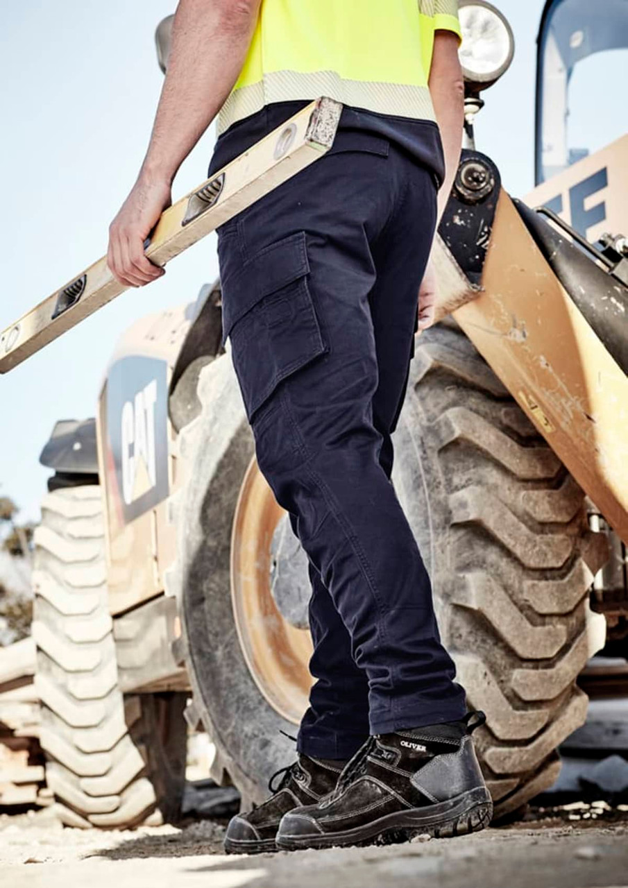 Curved cargo pants in navy, featuring multiple pockets, worn by a person holding a level near a machinery backdrop.