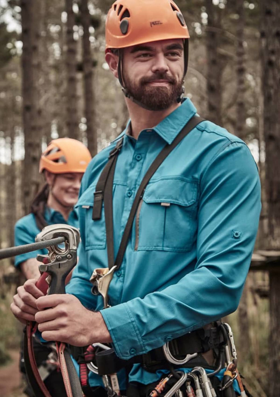 A blue long sleeve button-up shirt worn by a man, in a forest setting, with climbing gear and a helmet.