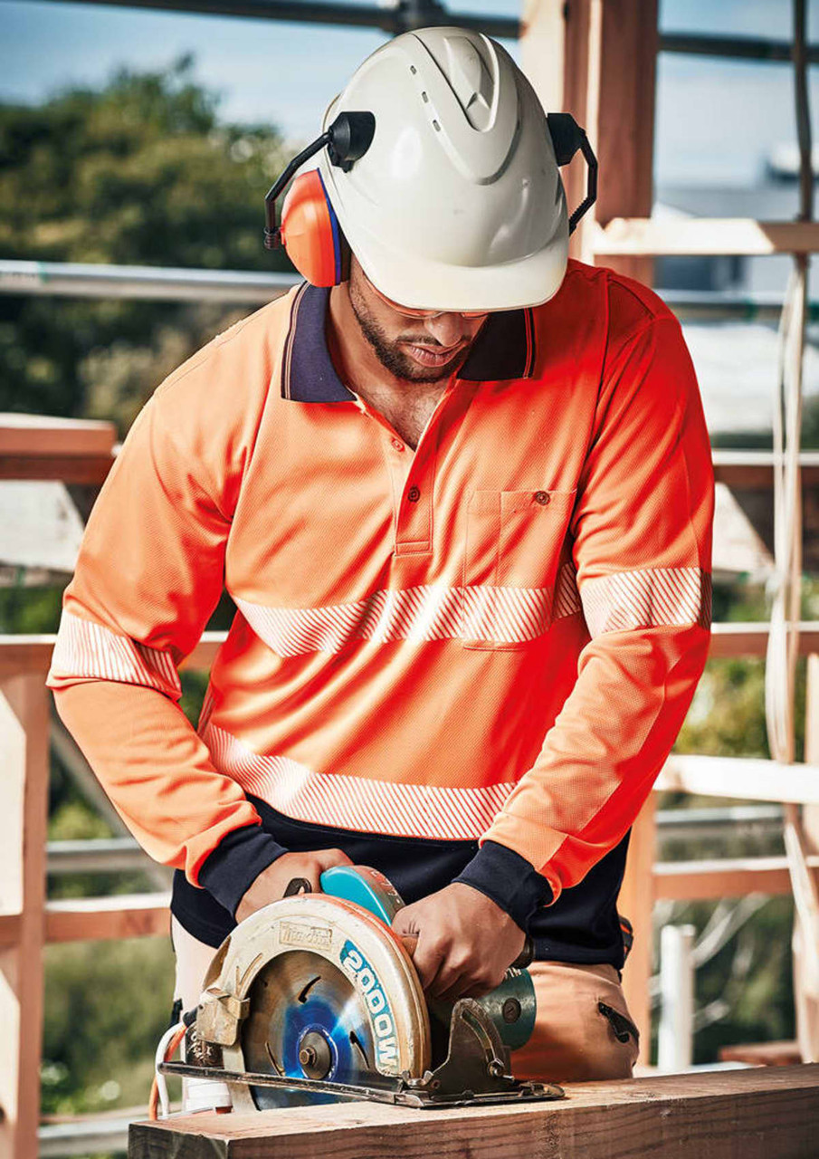 A person wearing an orange long sleeve polo shirt with segmented reflective tape operates a circular saw, wearing a helmet and ear protection.