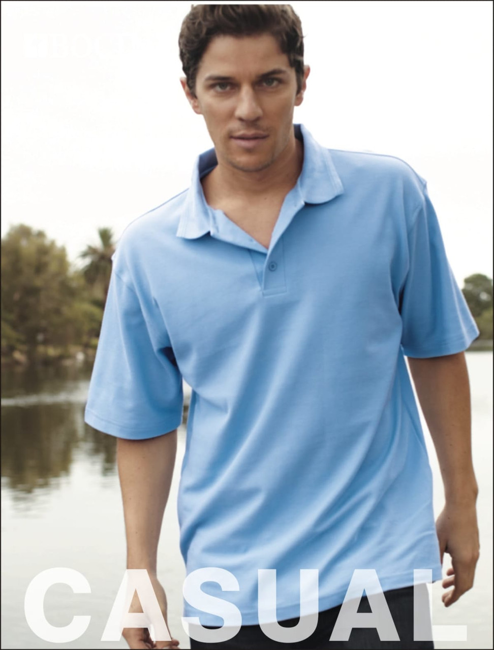 A light blue unisex polo shirt with a collar, being worn by a model outdoors near water.